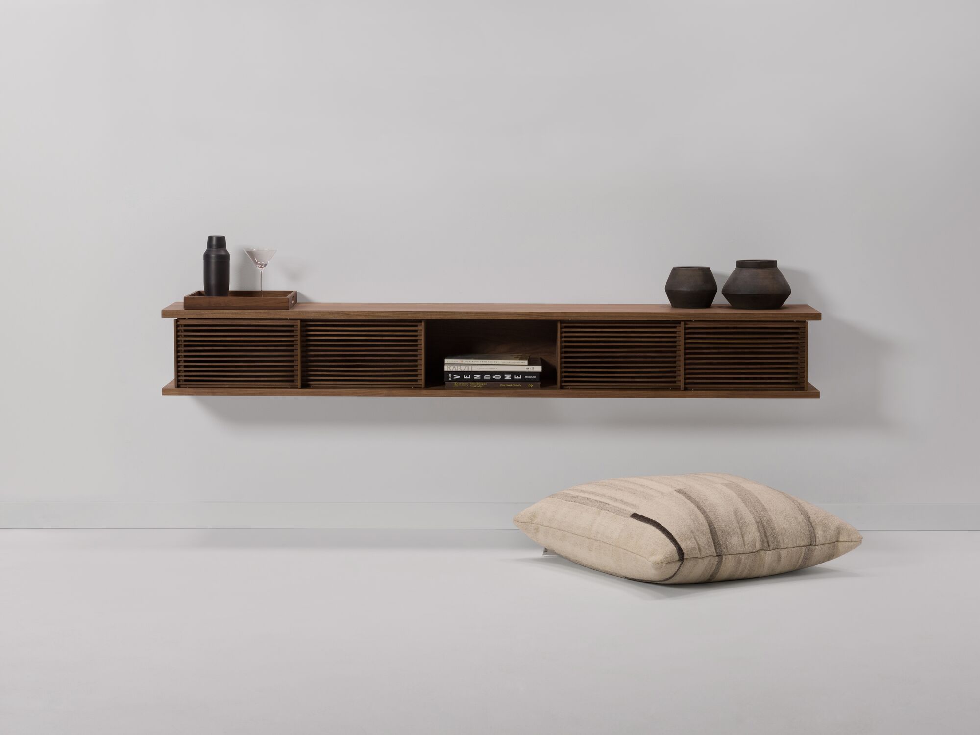 Large walnut floating wall shelf with vases on it and floor pillow beside it